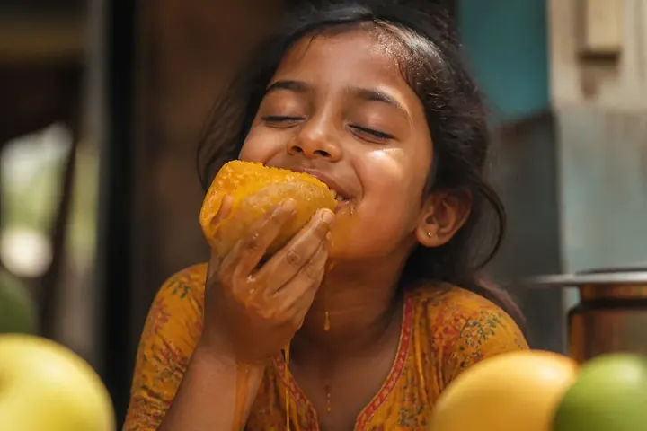 favorite meaning picture: A happy child biting into a ripe mango with juice running down her chin