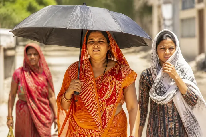 heat meaning picture: People in India shading themselves with umbrellas and scarves on a blazing hot summer afternoon