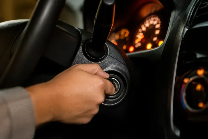 ignite meaning picture: Close-up of a hand turning a key in a car's ignition, dashboard lights glowing